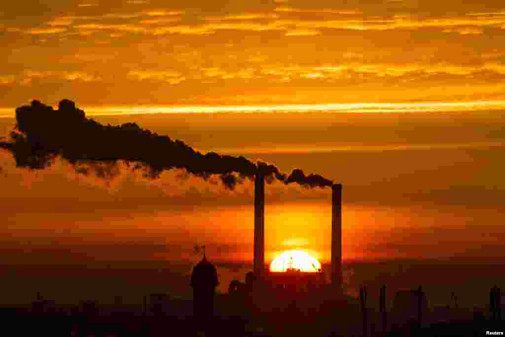 The sun rises behind the billowing chimneys of a power station in Berlin, Germany.