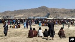 Hundreds of people gather near a U.S. Air Force C-17 transport plane at a perimeter at the international airport in Kabul, Afghanistan, Monday, Aug. 16, 2021. 