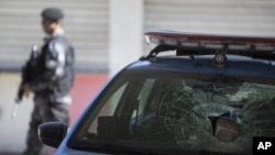 A police officer walks past police cruiser that had its windshield smashed by a brick after a confrontation with armed criminals at the Mangueira slum in Rio de Janeiro, Brazil, Aug. 11, 2015.