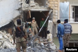 A civil defense member gestures towards a rebel fighter as they search for survivors at a site hit by what activists said were airstrikes carried out by the Russian Air Force in Idlib city, Syria Dec. 20, 2015.