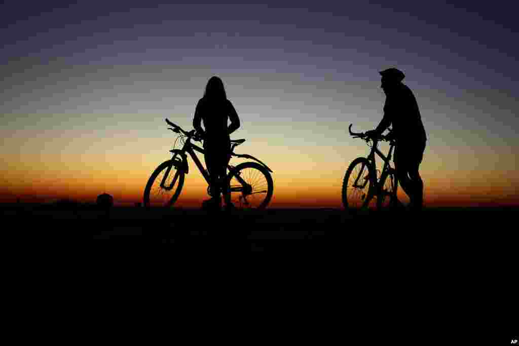 Bicyclists watch the colorful sky while waiting for the sun to rise, in Munich, Germany.