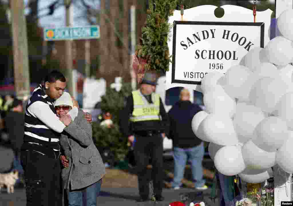 People grieve next to a makeshift memorial of flowers and balloons next to the Sandy Hook Elementary school sign in Sandy Hook, Connecticut, Dec. 15, 2012.