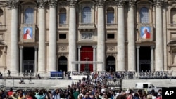 The tapestries showing the late Pope John Paul II and Pope John XXIII hang from the facade of St. Peter's Basilica as faithful and pilgrims crowd St. Peter's Square, April 25, 2014.