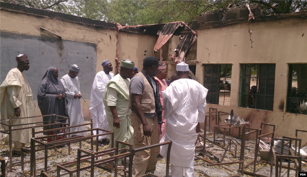 O Governador de Chibok (vestido de rosa), o comissário local para a educação (o quarto a partir da esquerda) com a segurança armada e residentes de Chibok, inspeccionam a escola que foi incendiada depois de mais de 200 terem sido raptadas por homens armados,&nbsp; Chibok, Nigéria, Abril 21, 2014. (Anne Look/VOA)