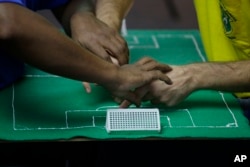 Carlos Junior, left, experiences the World Cup match between Brazil and Mexico with the help of an interpreter who uses tactile signing and a model soccer field to recount the game.