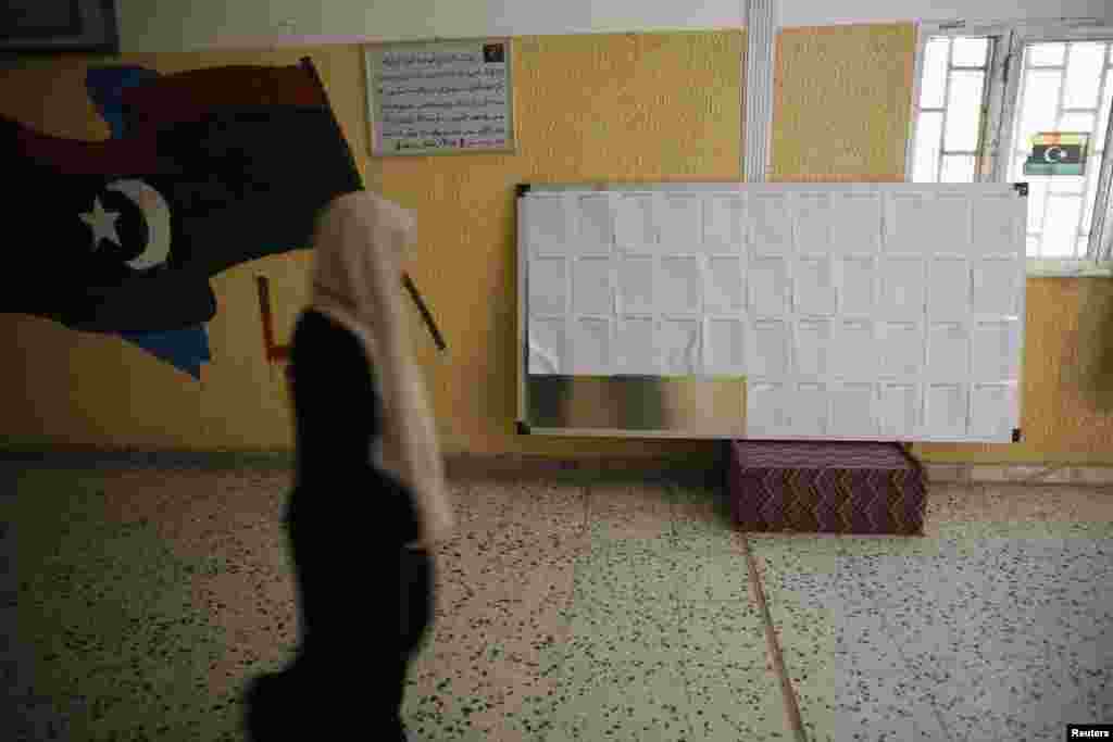 Seorang petugas pemilu melewati papan pendaftaran peserta pemilu di sebuah sekolah yang menjadi TPS di Tripoli (24/6). 