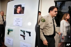 FILE- This May 24, 2014, photo shows Santa Barbara County Sheriff Bill Brown, right, after a news conference as he walks past a board showing photos of gunman Elliot Rodger and the weapons he used in a mass shooting the day before in Isla Vista, Calif. Authorities later concluded after an investigation that Rodger, who killed six people and injured 14 others, then killed himself, had acted alone.