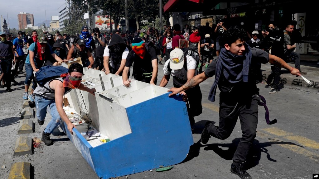 Manifestantes en Chile arrastran un mueble sacado de un negocio para usarlo como barricada en uno de los puntos de protesta en la capital. AP