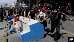 Manifestantes en Chile arrastran un mueble sacado de un negocio para usarlo como barricada en uno de los puntos de protesta en la capital. AP