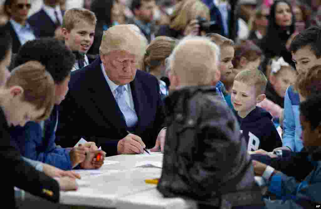 Presiden Donald Trump duduk bersama anak-anak menulis kartu-kartu ucapan untuk para prajurit di Gedung Putih, 2 April 2018, dalam acara tahunan Balap Telur Paskah.