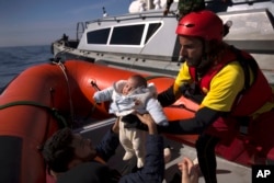 FILE - A 2-month-old baby from Libya is taken from a Libyan coast guard ship and loaded into a rubber rescue craft by members of the Spanish NGO Proactiva Open Arms, after being rescued from a wooden boat sailing out of control in the Mediterranean Sea.