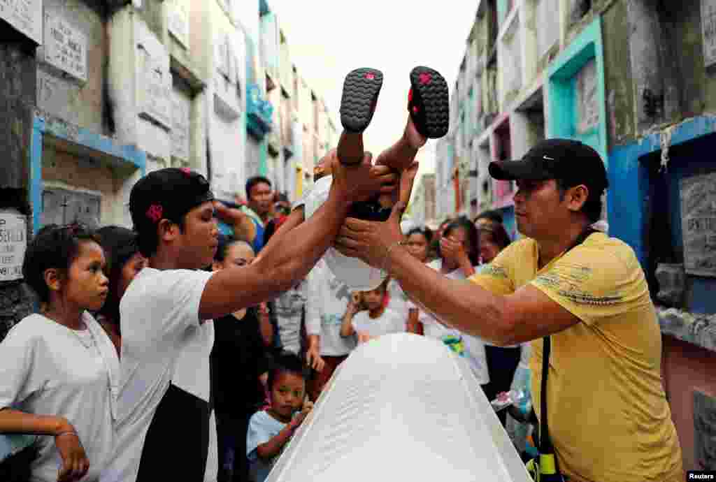 필리핀 나보스타스에서 고인의 영혼을 쉬게 해주기 위한 관습에 따라 유족들이 아이를 관 위로 들어올리고 있다.