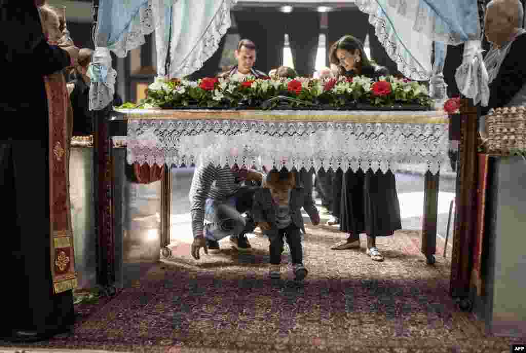 An Orhtodox priest blesses a child passing under a table which symbolizes the grave of Jesus Christ during the Good Friday processions at the main Orthodox church St Kliment in Skopje, Macedonia.