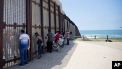 In this May 1, 2016 picture, Eva Lara, second from let, reacts as she reaches for her grandmother Juana Lara through the border wall during a brief visitation near where Mexico and the United States meet at the Pacific Ocean in San Diego. 