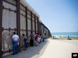 In this May 1, 2016, photo, Eva Lara, second from left, reacts as she reaches for her grandmother, Juana Lara, through the border wall during a brief visitation near where Mexico and the United States meet at the Pacific Ocean in San Diego.