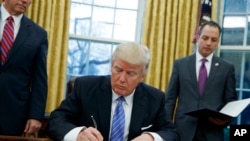 In this photo taken Monday, Jan. 23, 2017, President Donald Trump signs an executive order to withdraw the U.S. from the 12-nation Trans-Pacific Partnership trade in the Oval Office of the White House.