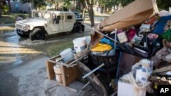A military vehicle passes flood-damaged belongings piled on a homeowners' front lawn in the aftermath of Hurricane Harvey at the Canyon Gate community in Katy, Texas, Sept. 7, 2017.