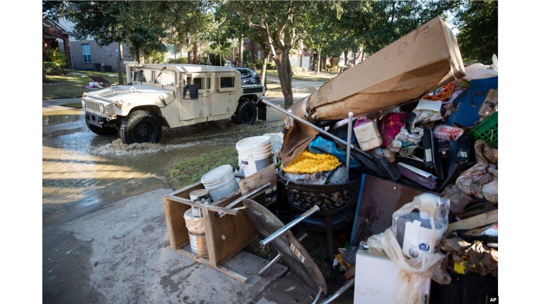 FILE - A military vehicle passes flood-damaged belongings piled on a homeowners' front lawn in the aftermath of Hurricane Harvey at the Canyon Gate community in Katy, Texas, Sept. 7, 2017.