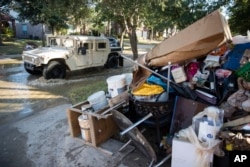 FILE - A military vehicle passes flood-damaged belongings piled on a homeowners' front lawn in the aftermath of Hurricane Harvey at the Canyon Gate community in Katy, Texas, Sept. 7, 2017.