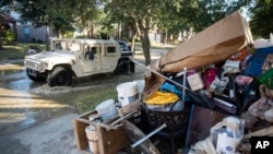 A military vehicle passes flood-damaged belongings piled on a homeowners' front lawn in the aftermath of Hurricane Harvey at the Canyon Gate community in Katy, Texas, Sept. 7, 2017.
