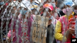 Cambodian garment workers shout slogans behind barbed wire set up by police near the Council of Ministers building during a rally in Phnom Penh, Cambodia, Monday, Dec. 30, 2013. The workers are demanding a raise in their monthly salary from US $160 to $80. (AP Photo/Heng Sinith)