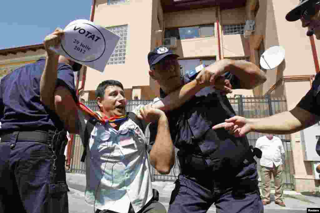 نقل مکان یک معترض توسط پلیس ضد شورش در مقابل ستاد به حالت تعلیق درآمده «ترايان باسسکو»، رئیس جمهوری رومانی، در شهر بخارست. دادگاه قانون اساسی رومانی رفراندوم برای استیضاح باسسکو را رد کرد. اين امر تلاش ها