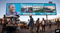 FILE - People walk under a giant poster showing Democratic Republic of the Congo's President and candidate for a second term Joseph Kabila, in Kinshasa, Nov. 7, 2011.