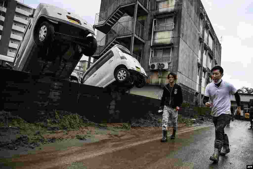 Men walk past cars upended by recent floods in Hitoyoshi, Kumamoto prefecture in Japan, after heavy rains and flooding devastated the region. 