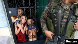 Children watch police officers as they paint over graffiti related to the MS-13 gang in the La Vega neighborhood in San Salvador, El Salvador, Sept. 26, 2017.