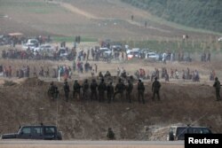 Israeli soldiers are seen next to the border fence on the Israeli side of the Israel-Gaza border as Palestinians protest on the Gaza side of the border, Oct. 19, 2018.