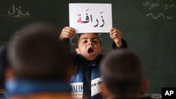 A Syrian refugee boy holds up a placard in Arabic, during class at a remedial education center run by Relief International in the Zaatari Refugee Camp, near Mafraq, Jordan, Jan. 21, 2016.
