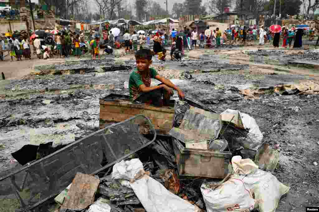A Rohingya refugee boy sits on a stack of burned material after a massive fire broke out and destroyed thousands of shelters in a Rohingya refugee camp in Cox's Bazar, Bangladesh.