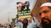 FILE - A supporter of Islamic charity organization Jamaat-ud-Dawa (JuD) carries a sign with others as they listen to the speech of leaders (unseen) to condemn the house arrest of Hafiz Saeed, chief of (JuD) during a protest demonstration in Karachi, Pakistan, Feb. 3, 2017. 