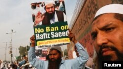 FILE - A supporter of Islamic charity organization Jamaat-ud-Dawa (JuD), carries a sign with others as they listen the speech of leaders (unseen) to condemn the house arrest of Hafiz Muhammad Saeed, chief of (JuD), during a protest demonstration in Karachi, Pakistan, Feb. 3, 2017.