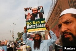 FILE - A supporter of Islamic charity organization Jamaat-ud-Dawa carries a sign with others as they listen the speech of leaders (unseen) condemning the house arrest of Hafiz Saeed, chief of JuD, during a demonstration in Karachi, Pakistan, Feb. 3, 2017.