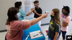 FILE - In this July 14, 2020, file photo, amid concerns of the spread of COVID-19, science teachers Ann Darby, left, and Rosa Herrera check-in students before a summer STEM camp at Wylie High School in Wylie, Texas. Schools and camps across the county are