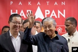 FILE - Malaysia's Prime Minister Mahathir Mohamad, center, waves next to newly appointed Finance Minister Lim Guan Eng, left, after a press conference to announce his cabinet members in Petaling Jaya, May 12, 2018.