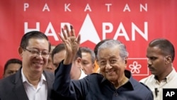 Malaysia's Prime Minister Mahathir Mohamad, center, waves next to newly appointed Finance Minister Lim Guan Eng, left, after a press conference to announce his cabinet members in Petaling Jaya, May 12, 2018. 