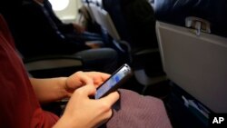 ARSIP – Seorang penumpang pesawat tampak memeriksa telepon selularnya sebelum tinggal landas dari Boston (foto: AP Photo/Matt Slocum, Arsip).