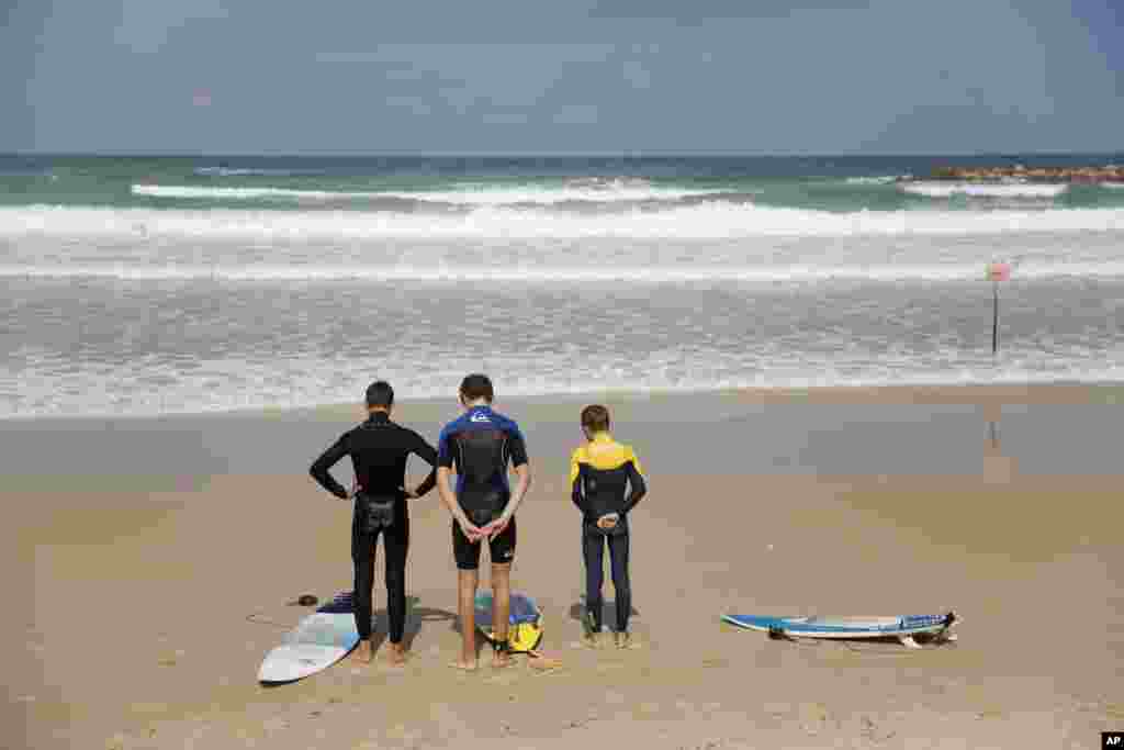 Surfers stand still on the Mediterranean Sea beachfront as a two-minute siren sounds in memory of victims of the Holocaust, in Netanya, Israel.