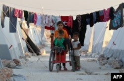 FILE - Displaced Syrian children push a boy with disability on makeshift wheelchair at a camp for displaced people in the northern Idlib province, Aug. 29, 2018.