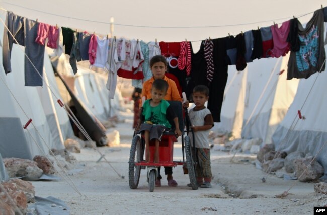 FILE - Displaced Syrian children push a boy with disability on makeshift wheelchair at a camp for displaced people in the northern Idlib province, Aug. 29, 2018.