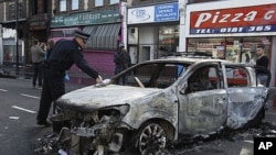 A police officer removes identification from a police car set on fire and burnt during riots in Tottenham, north London, August 7, 2011