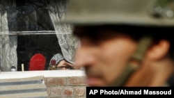 A Kashmiri woman watches from inside her home window an Indian policeman stand guard during a protest on the outskirts of Srinagar, India, Jan. 8, 2013.