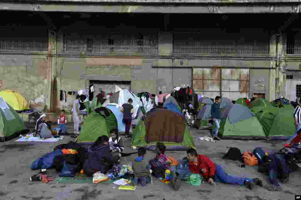 Refugees and migrants sit outside their tents at Athens&#39; port of Piraeus, Greece.