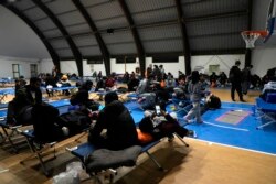 A group of refugees and migrants wait to leave a temporary shelter set in a gym in Monasterace, Calabria region, Southern Italy, Nov. 11, 2021.