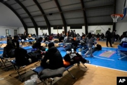 A group of refugees and migrants wait to leave a temporary shelter set in a gym in Monasterace, Calabria region, Southern Italy, Nov. 11, 2021.