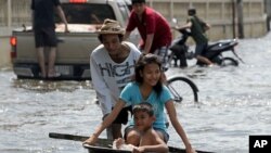 ຜູ້ຊາຍຄົນນຶ່ງພວມຍູ້ລູກຂອງລາວທີ່ນັ່ງຢູ່ໃນຊາມອ່າງໃຫຍ່ ໄປຕາມນໍ້າທີ່ຖ້ວມຂຶ້ນມາ ໃນເຂດບາງກອກ (21 ຕຸລາ 2011)