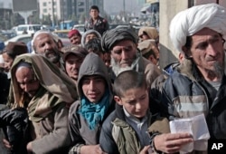 FILE - Afghan men and boys wait in line to receive their donated sacks of wheat distributed by the World Food Program in Kabul, Afghanistan, Dec. 15, 2013.