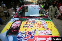 FILE - A resident walks past a parked car decorated with a poster of Mohammad Yaqoob Sheikh, candidate of the Milli Muslim League political party, during an election campaign for the National Assembly NA-120 constituency in Lahore, Pakistan, Sept. 9, 2017